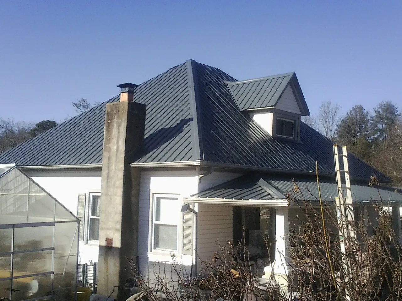 Dark blue standing seam metal roof on a white farmhouse with dormer — Slate & Tile Roof Repair by Roofing Brothers in Poulan