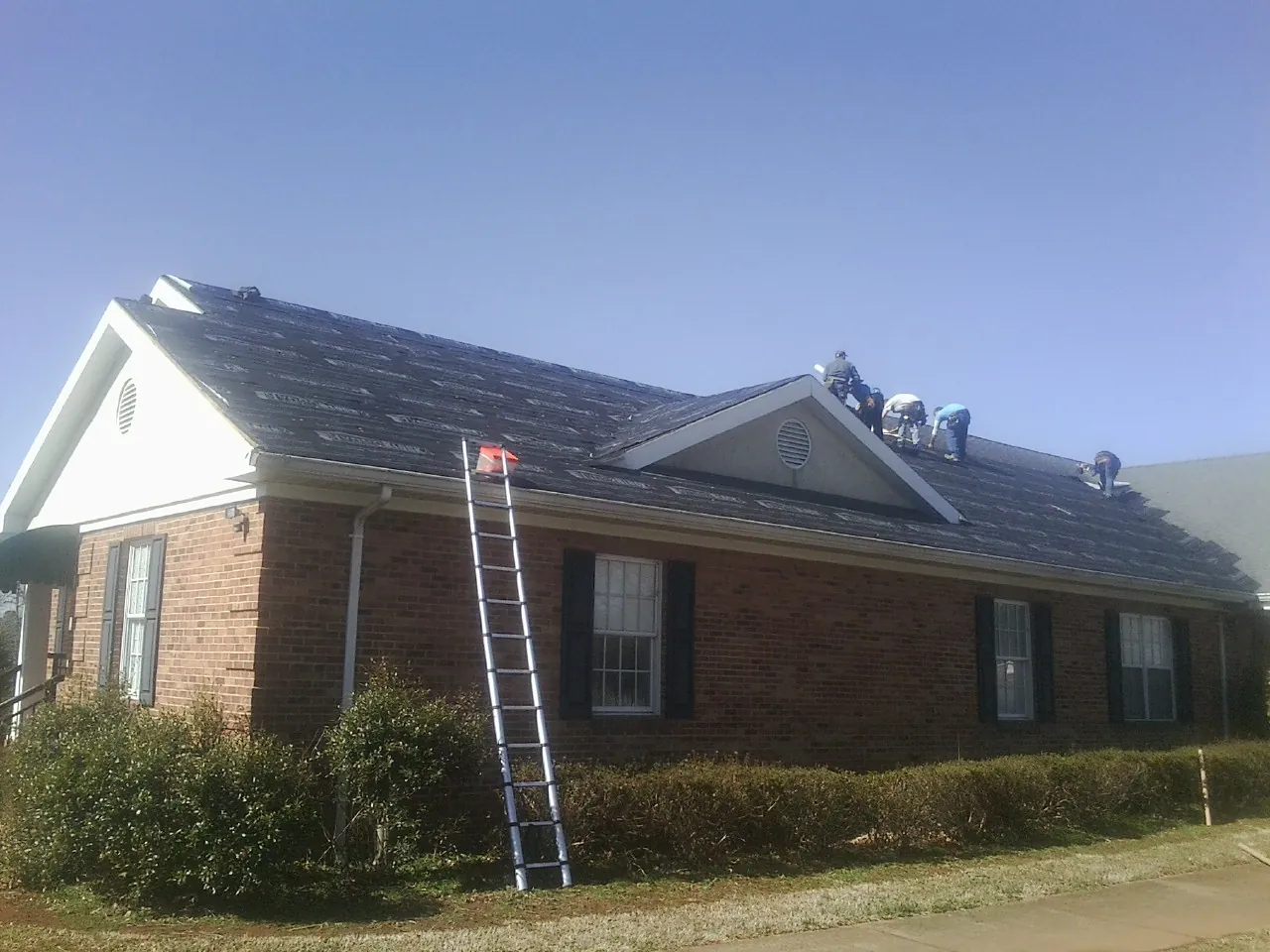 Crew tearing shingles off a brick ranch roof with a ladder set — Emergency Roof Repair work by our crew in Poulan