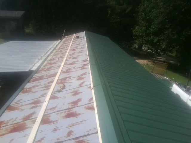 Old rusted panels beside newly installed green metal roofing — Wind Damage Roof Repair by Roofing Brothers in Poulan