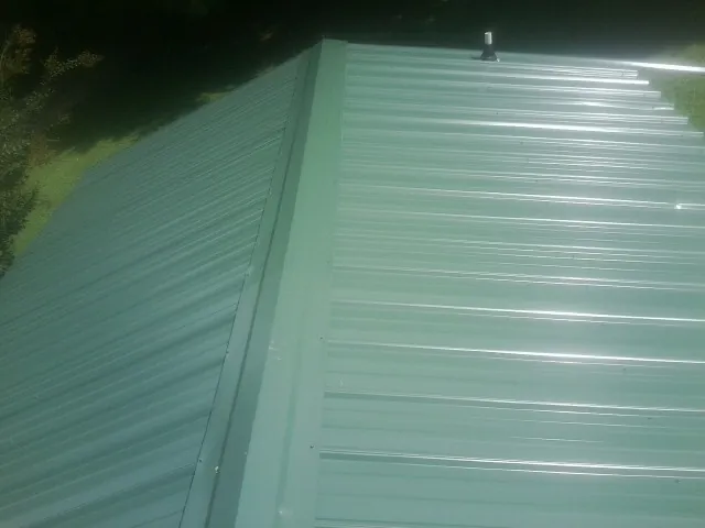 New green metal panels meeting at the ridge of a roof — Flat Roof Repair work by our crew in Poulan