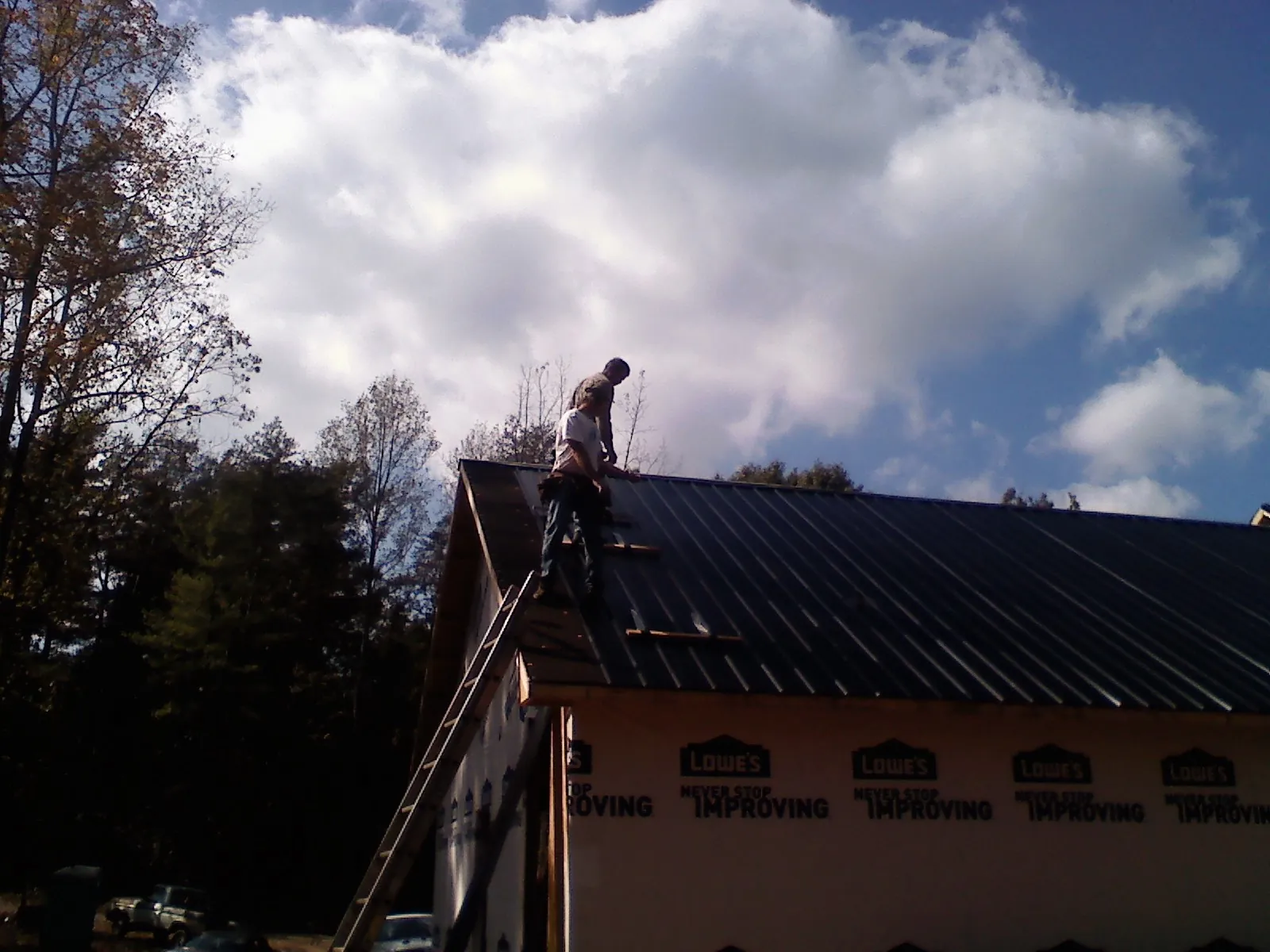 Roofer fastening dark metal panels high against a cloudy sky, from a Roof Inspection job in Poulan
