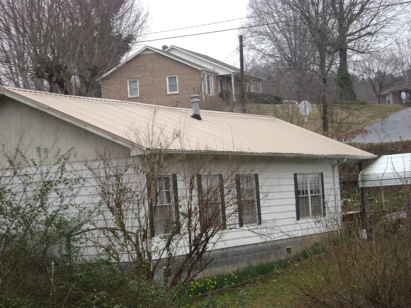 Tan metal roof on a white sided house set into a hillside — Commercial Roofing by Roofing Brothers in Poulan