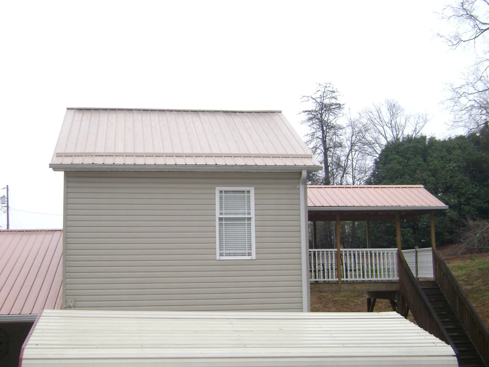 Tan metal roofs on a two story addition and attached porch, from a Roof Replacement job in Poulan